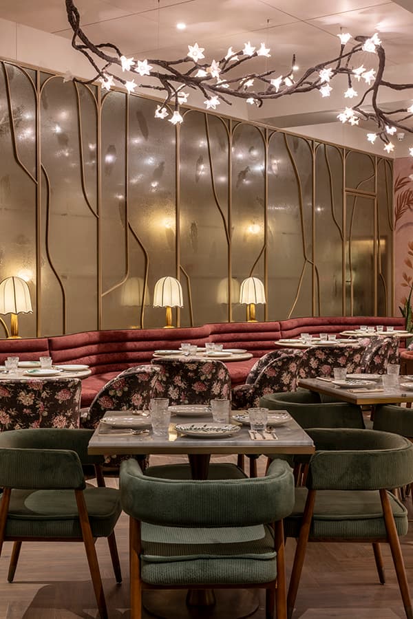 Red curved banquette with floral chairs beneath branch lighting