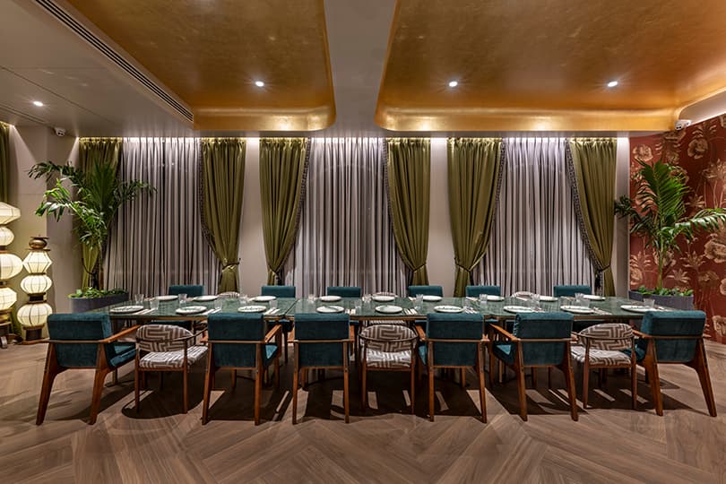 Long private dining table framed by olive curtains