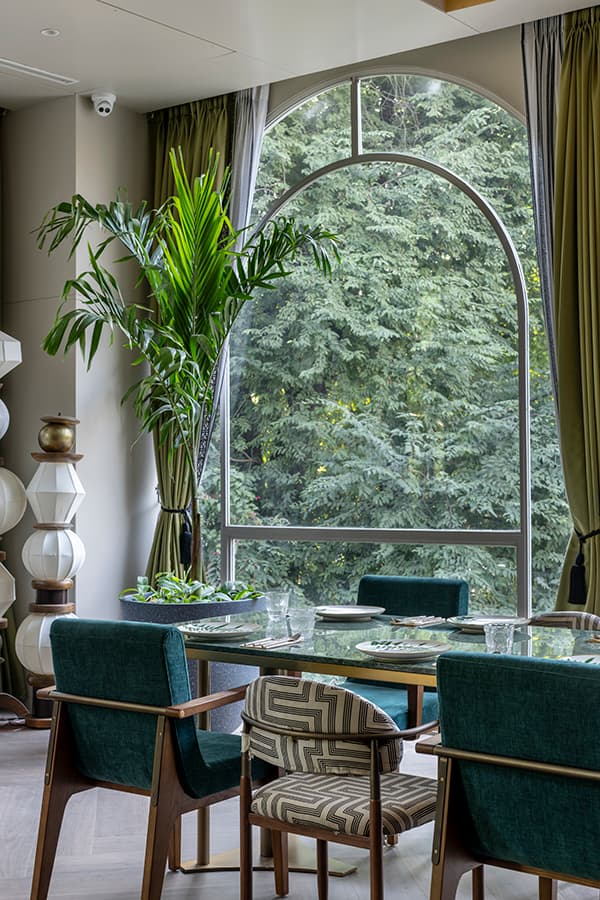 Arched window overlooking greenery beside a green-chaired table