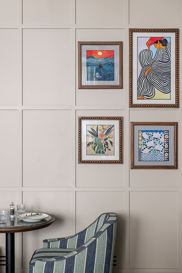 Framed prints above a small table and a striped chair