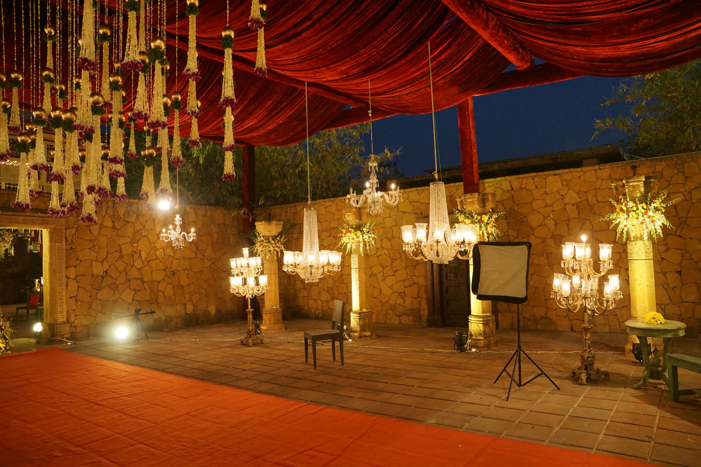 Red carpet beneath hanging chandeliers in a stone-walled courtyard
