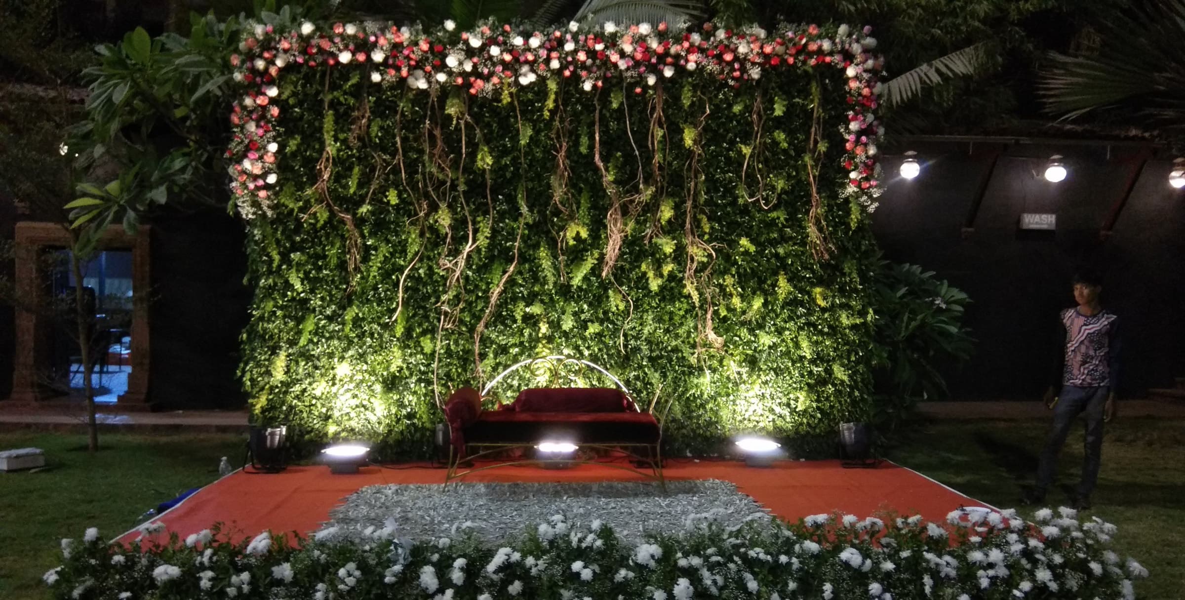 Green floral backdrop with white flowers and a red carpet stage