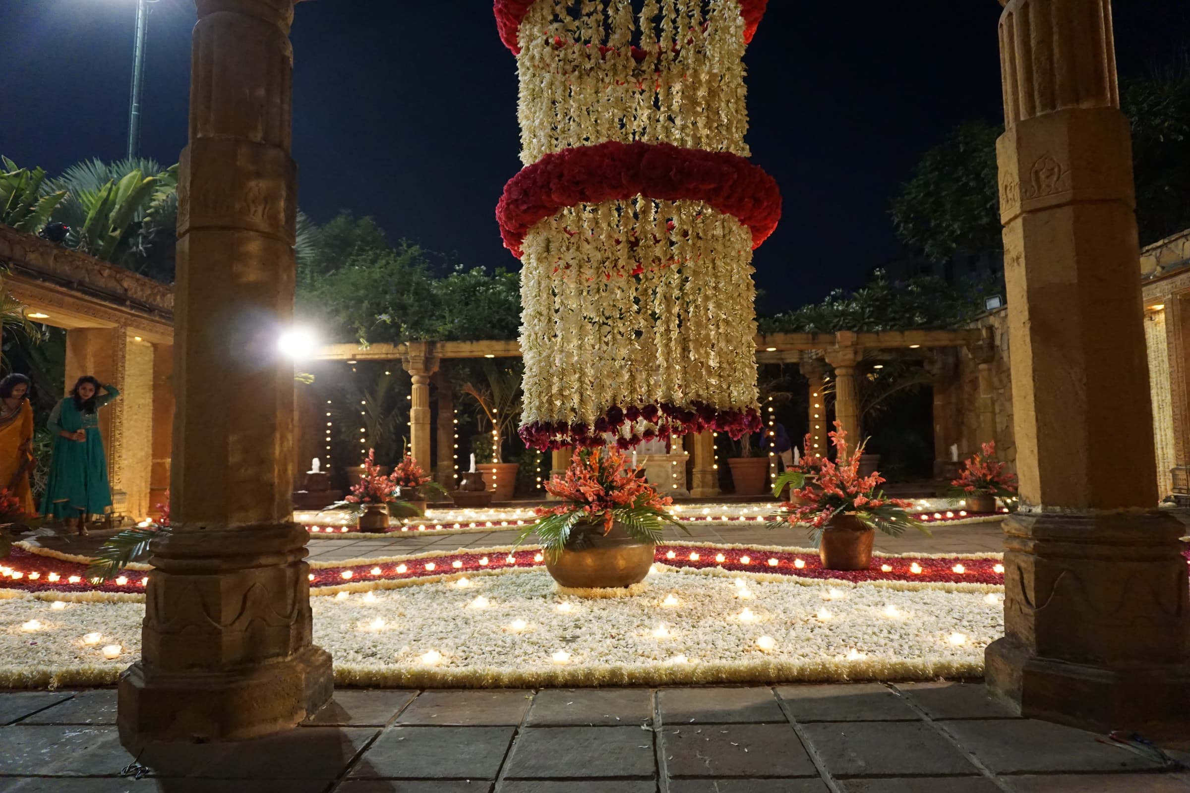 Tall floral column wrapped in garlands between stone pillars at night