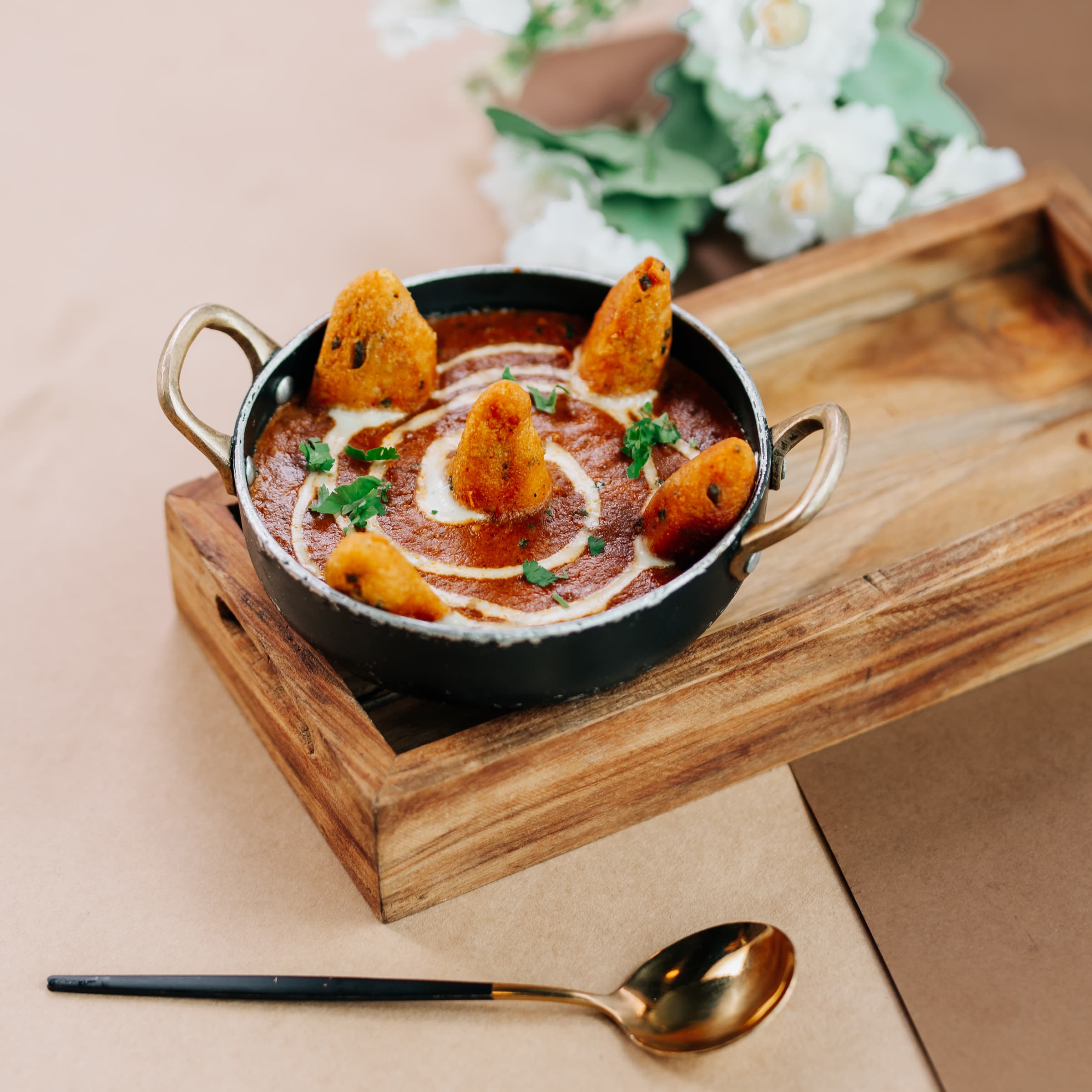 Kadai of curry with fried dumplings on a wooden tray