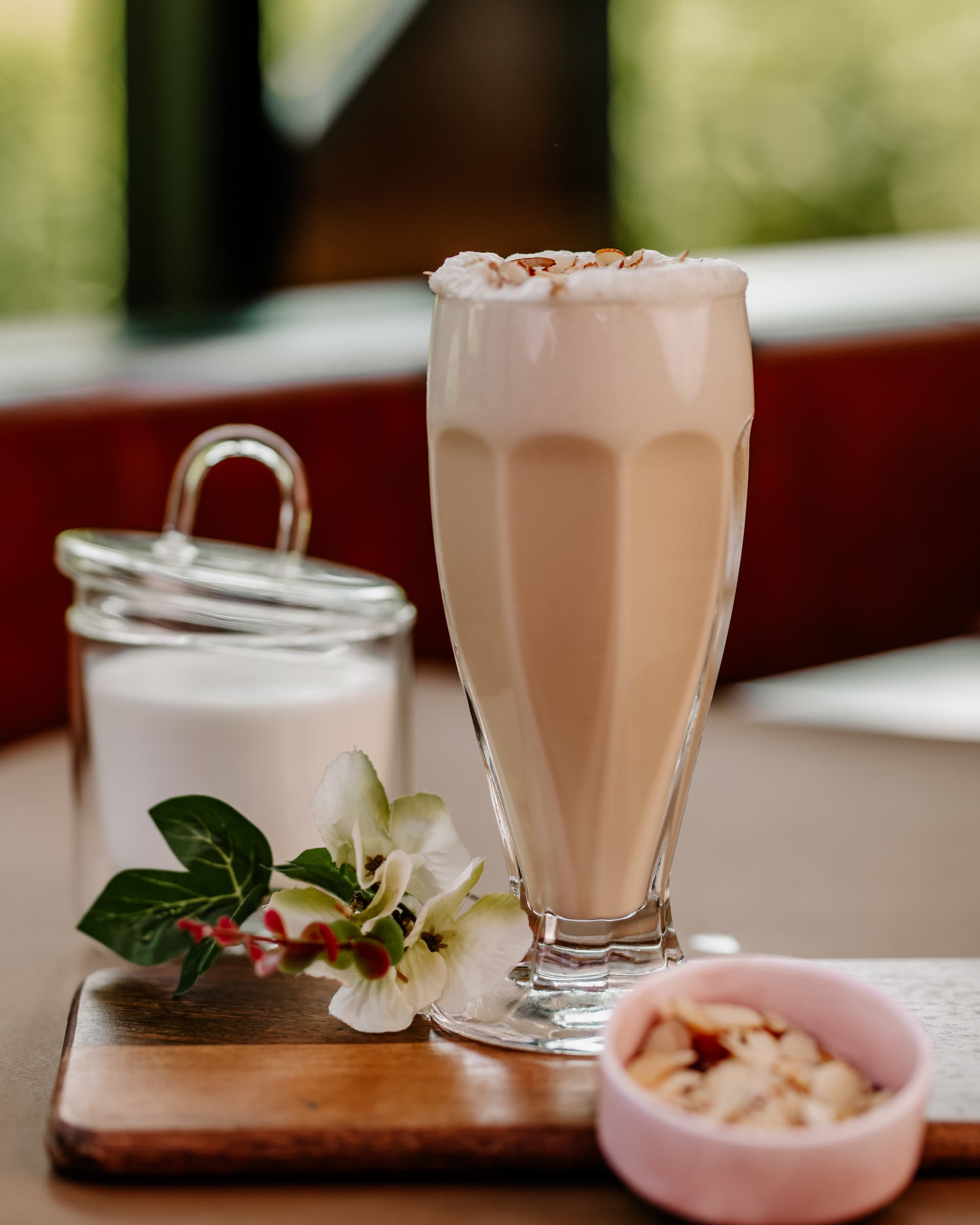 Chilled coffee shake in a tall glass with a sugar jar and almonds