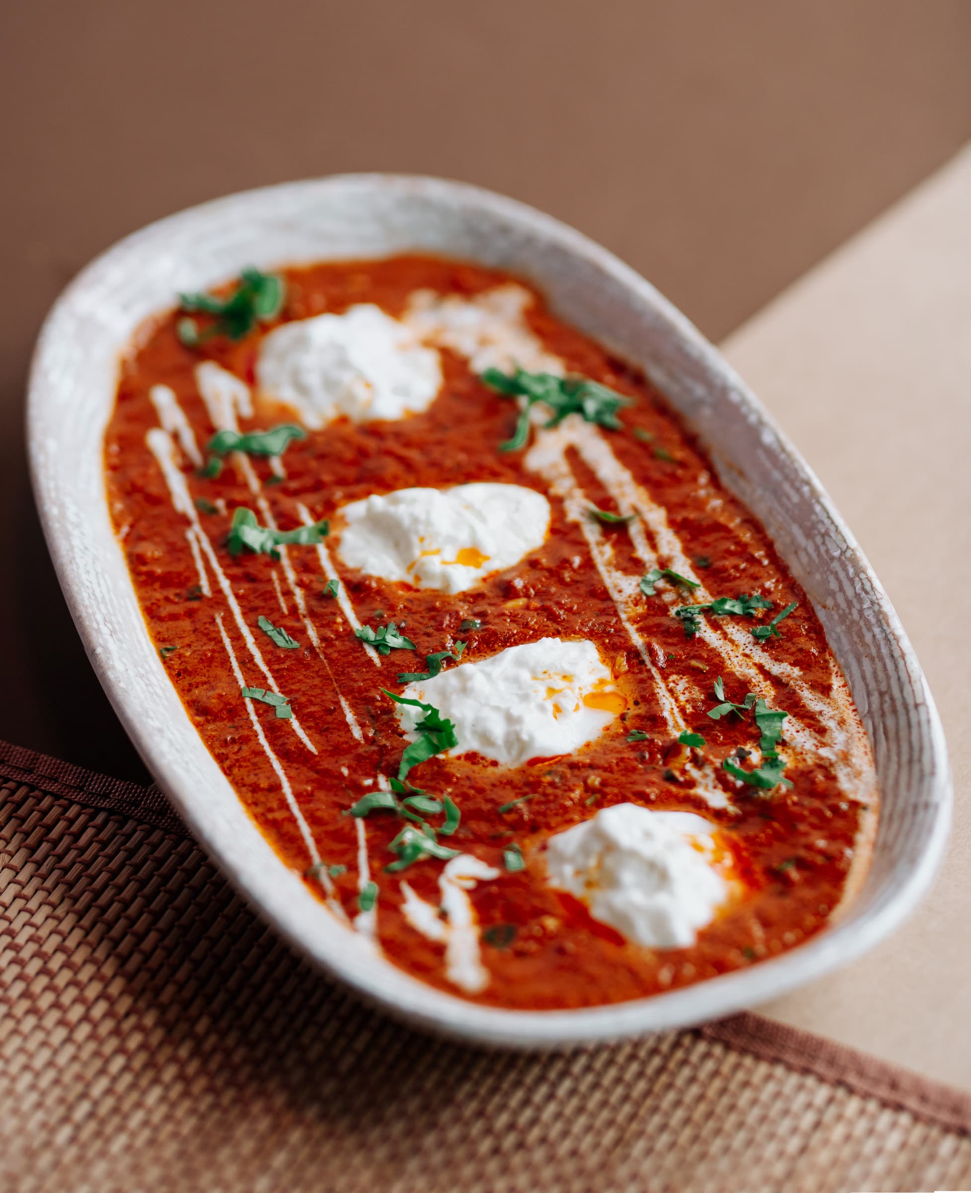 Tomato curry with cream dollops in an oval stone bowl