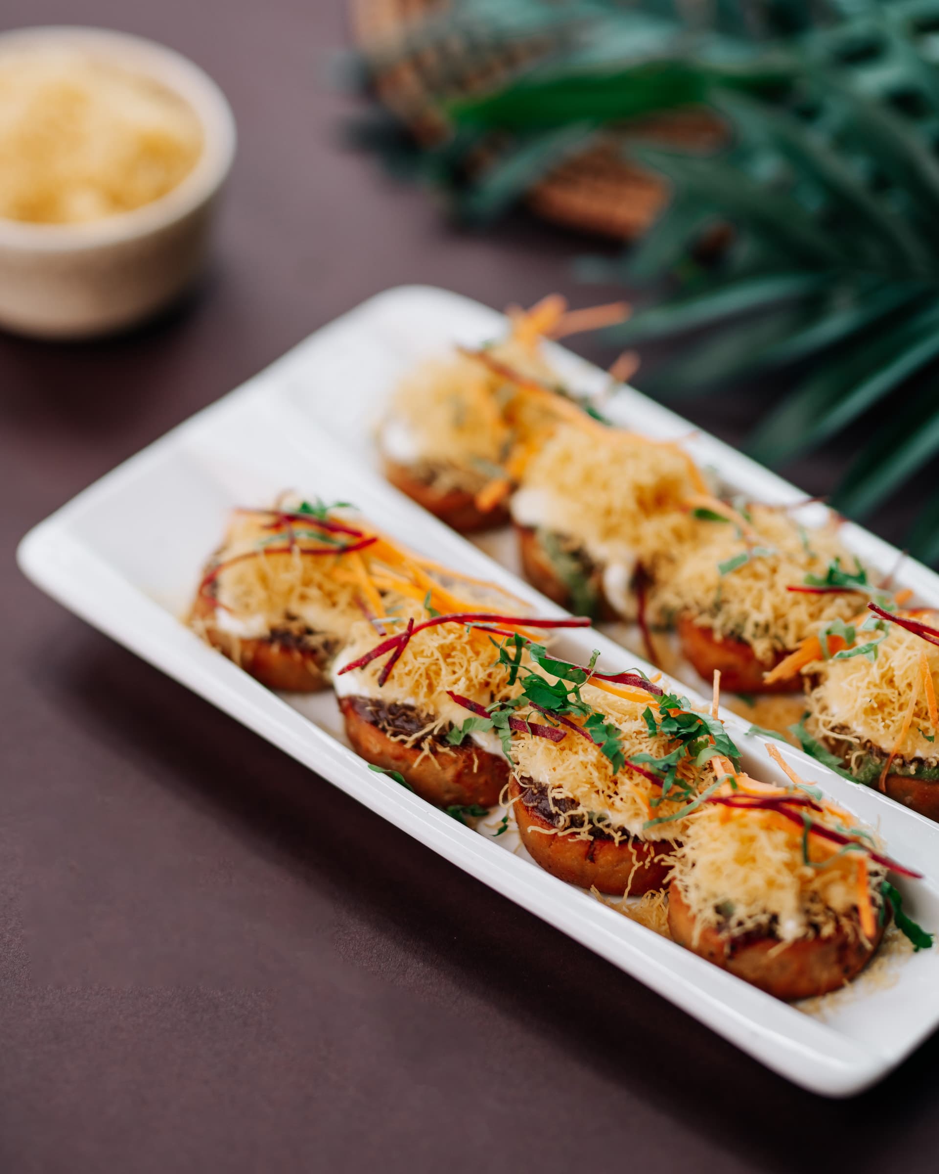 Cheese-topped toasts on a long white plate with a palm leaf