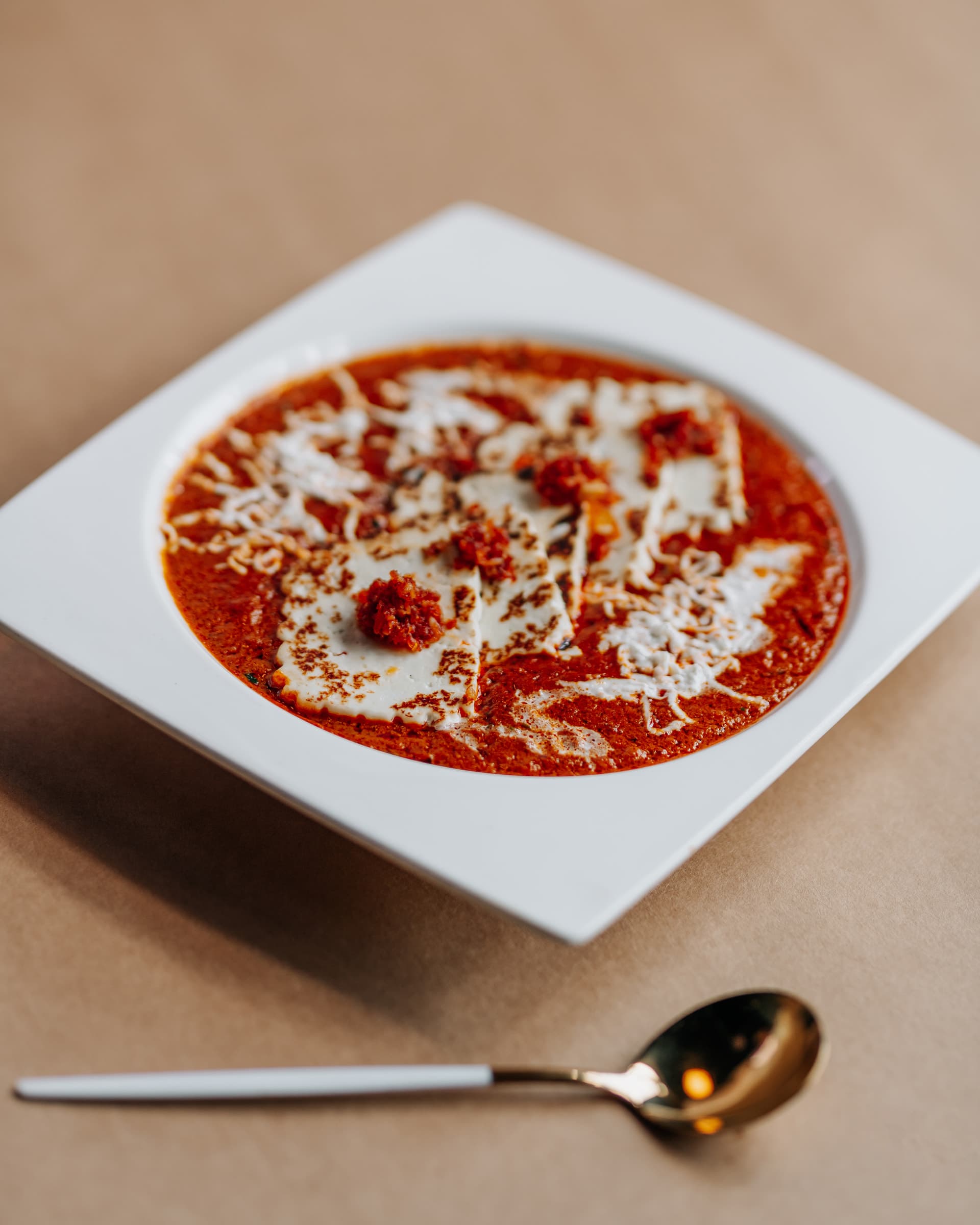 Tomato and cheese dish in a white square bowl with a gold spoon