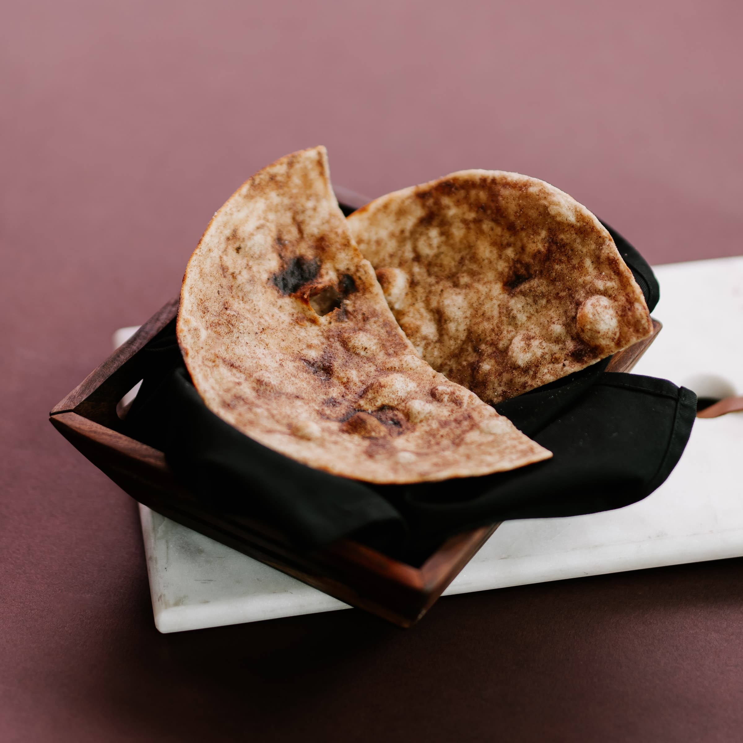 Flatbreads in a black-lined basket on a mauve backdrop