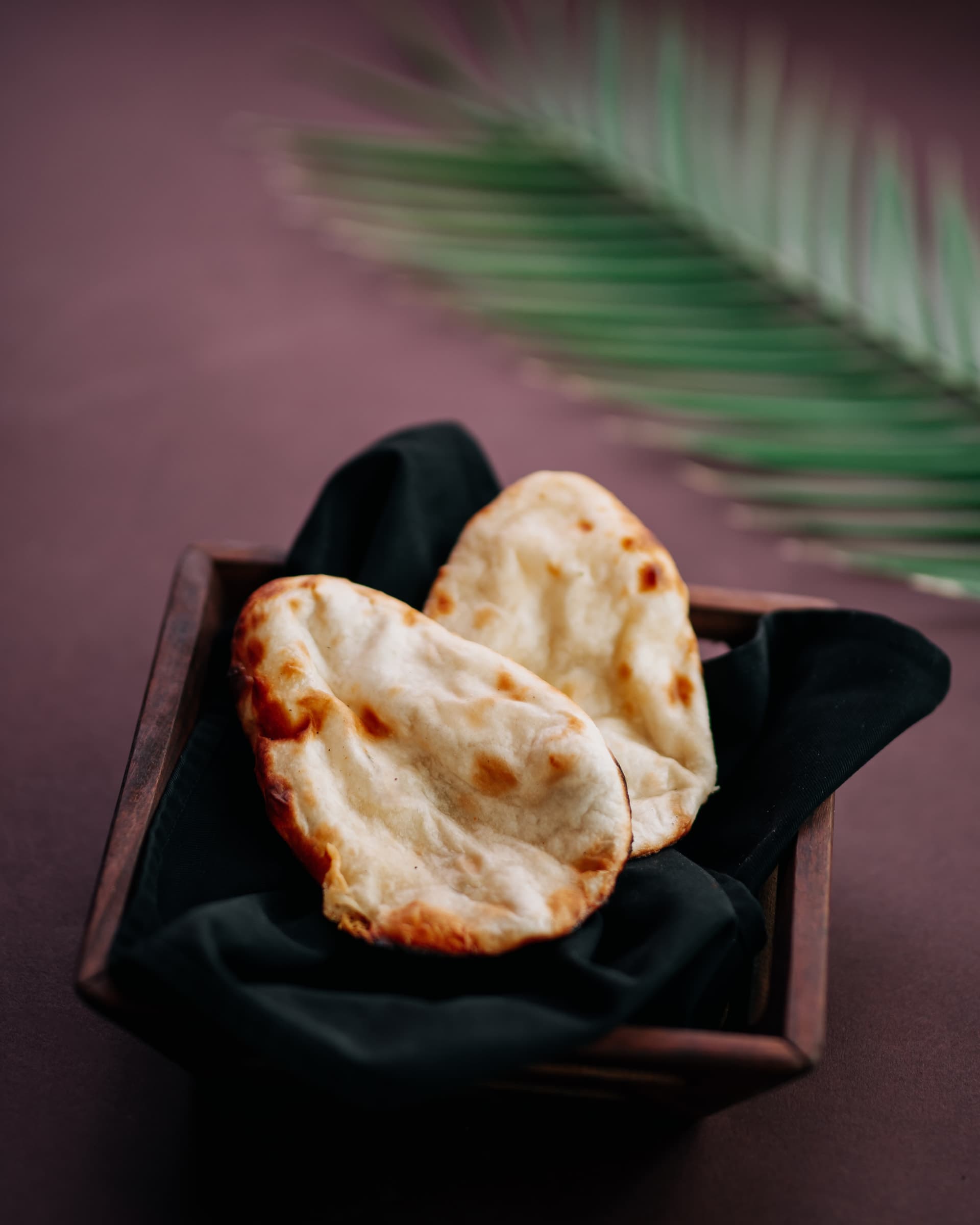 Naan in a dark basket beside a palm leaf