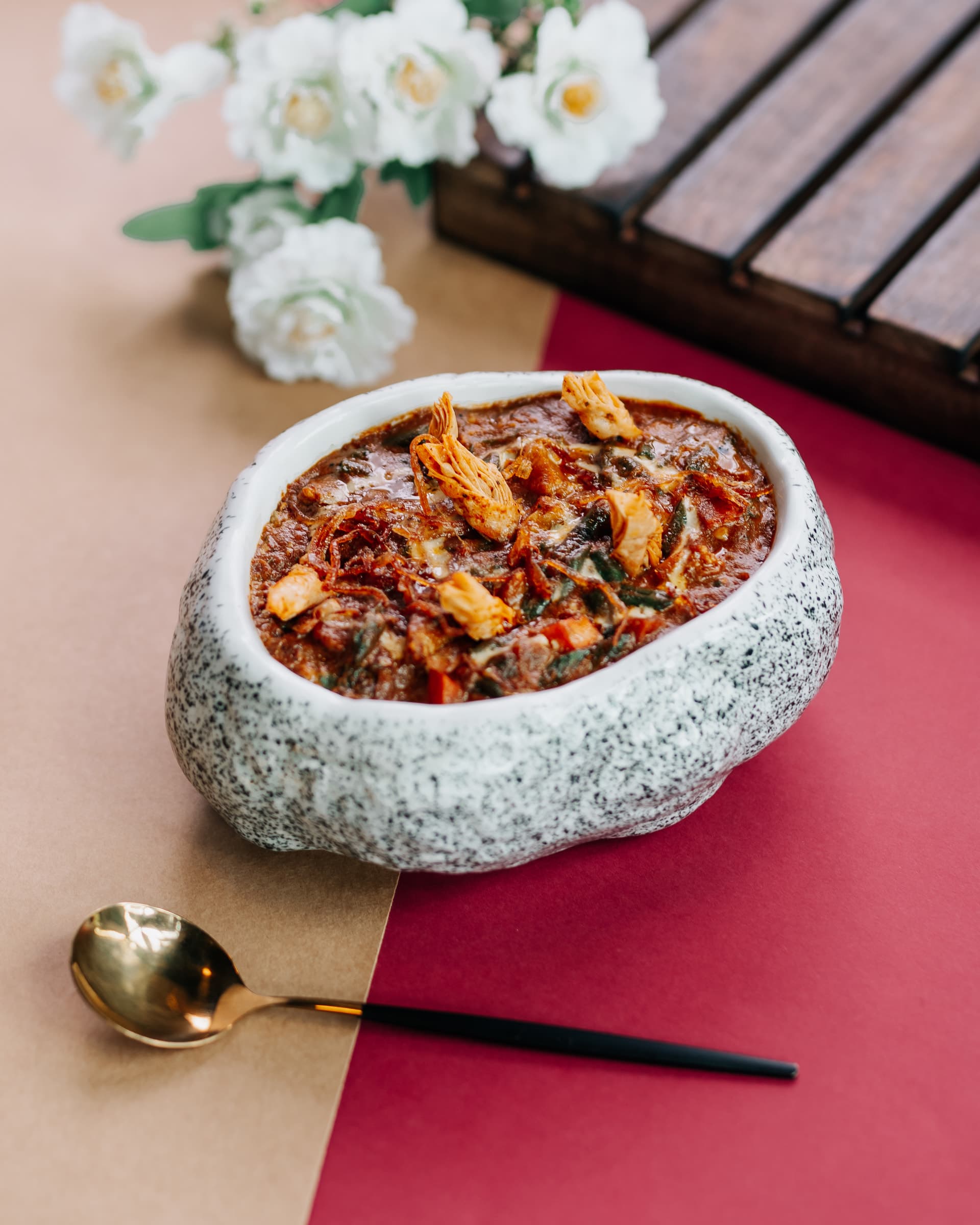 Curry in a speckled stone bowl beside white flowers
