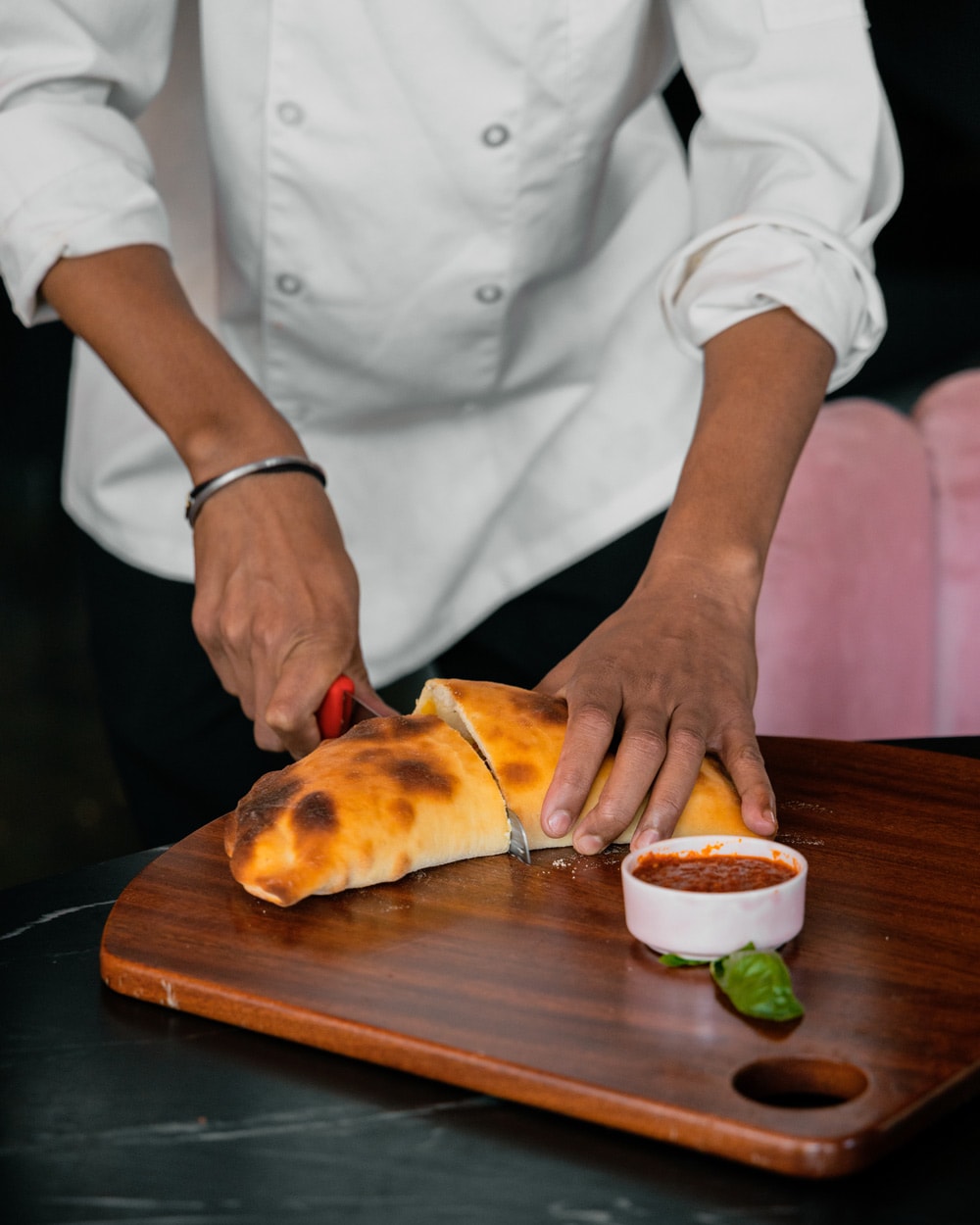 A chef slicing a mini calzone, plated with a dip