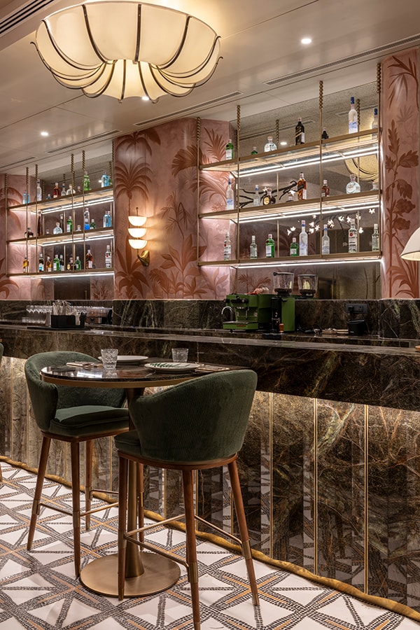Bar counter with green stools and a pink shelving wall