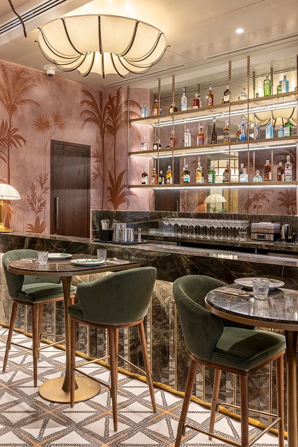 Illuminated bar shelves and chandelier over green bar stools