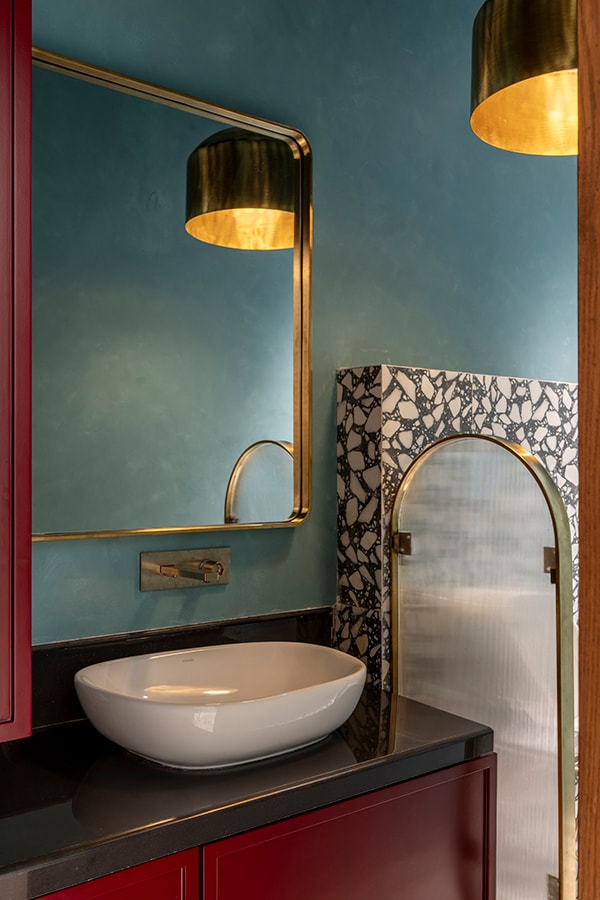 Powder room with teal walls, brass light and a red vanity