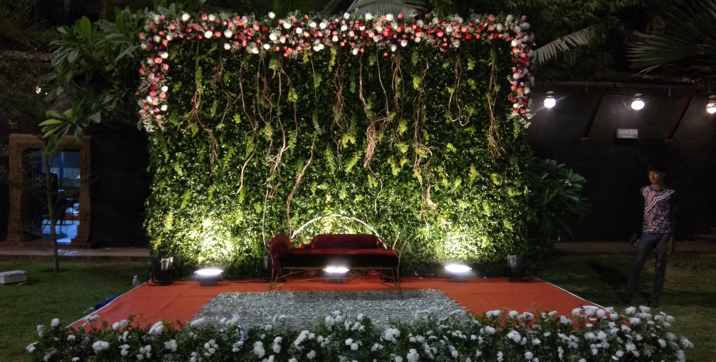 Green floral backdrop with white flowers and a red carpet stage