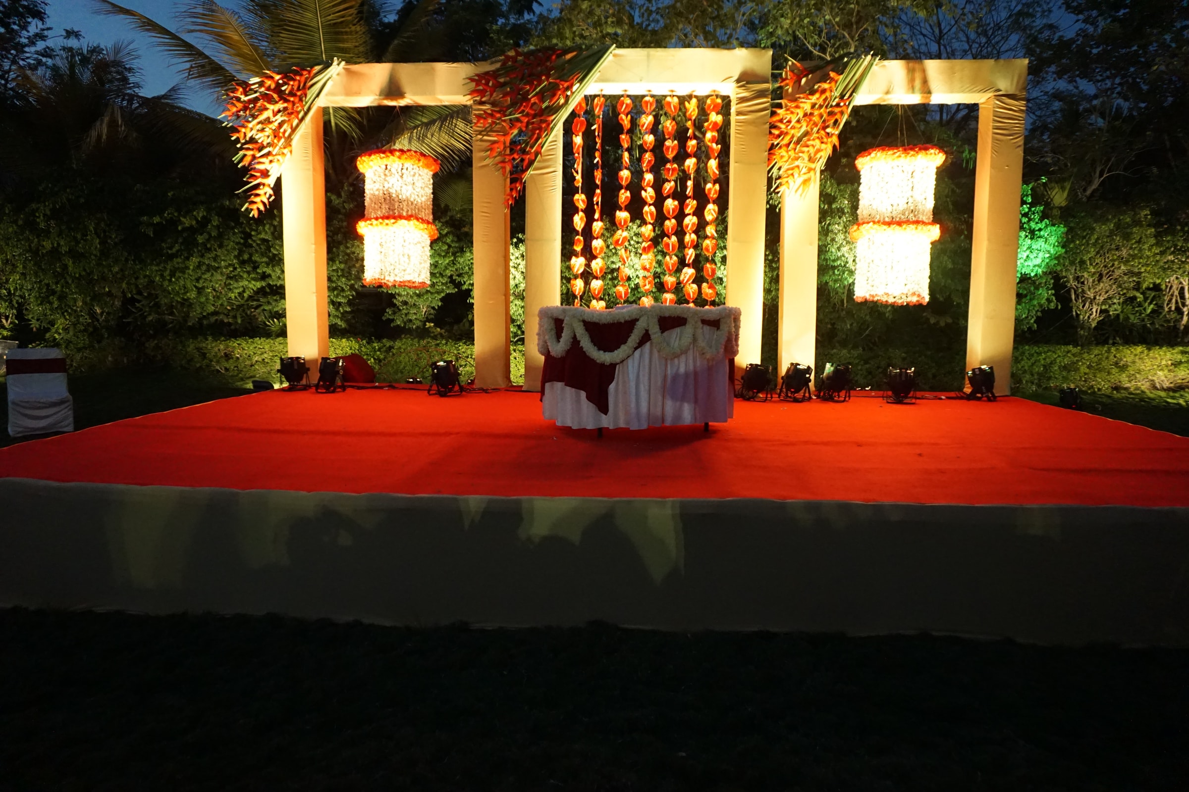 Illuminated timber-frame stage on a red carpet beneath palms