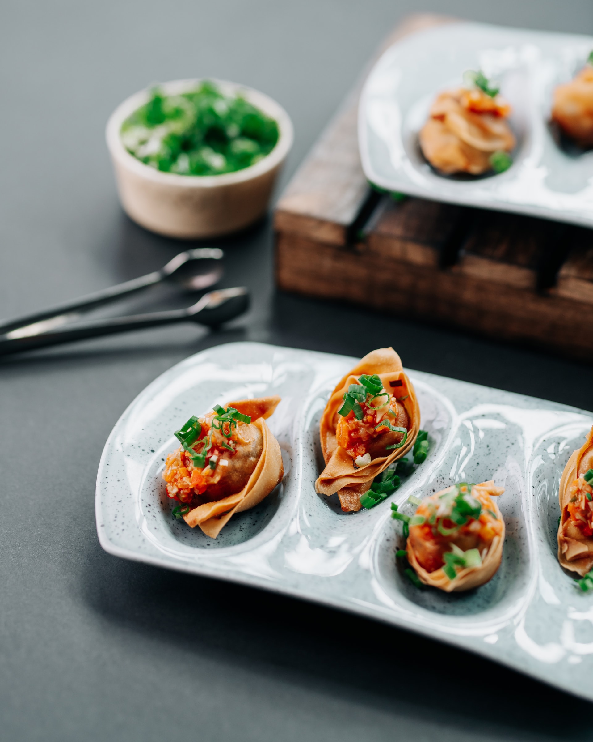 Filled tartlets in an oval dish beside a bowl of chives