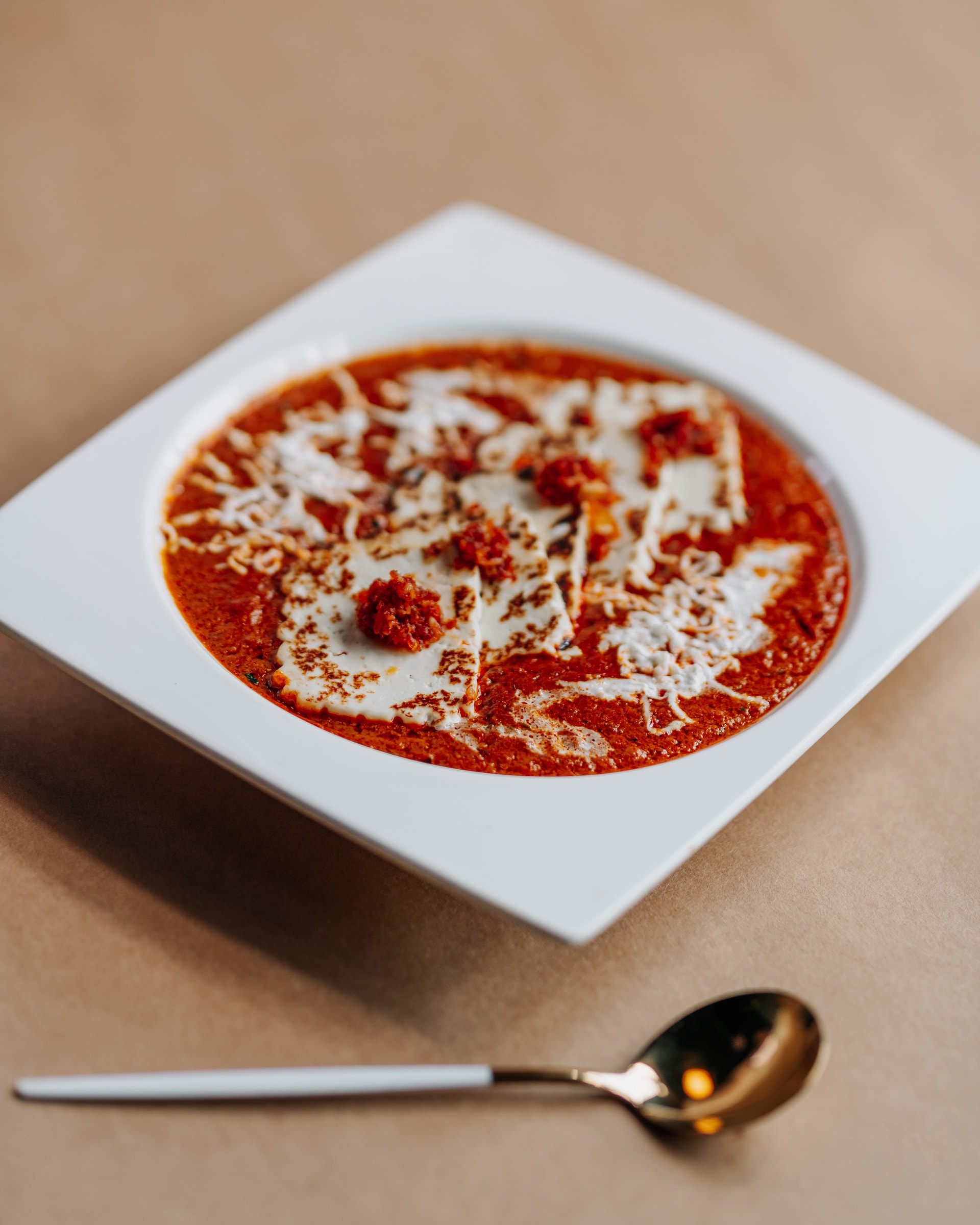 Tomato and cheese dish in a white square bowl with a gold spoon