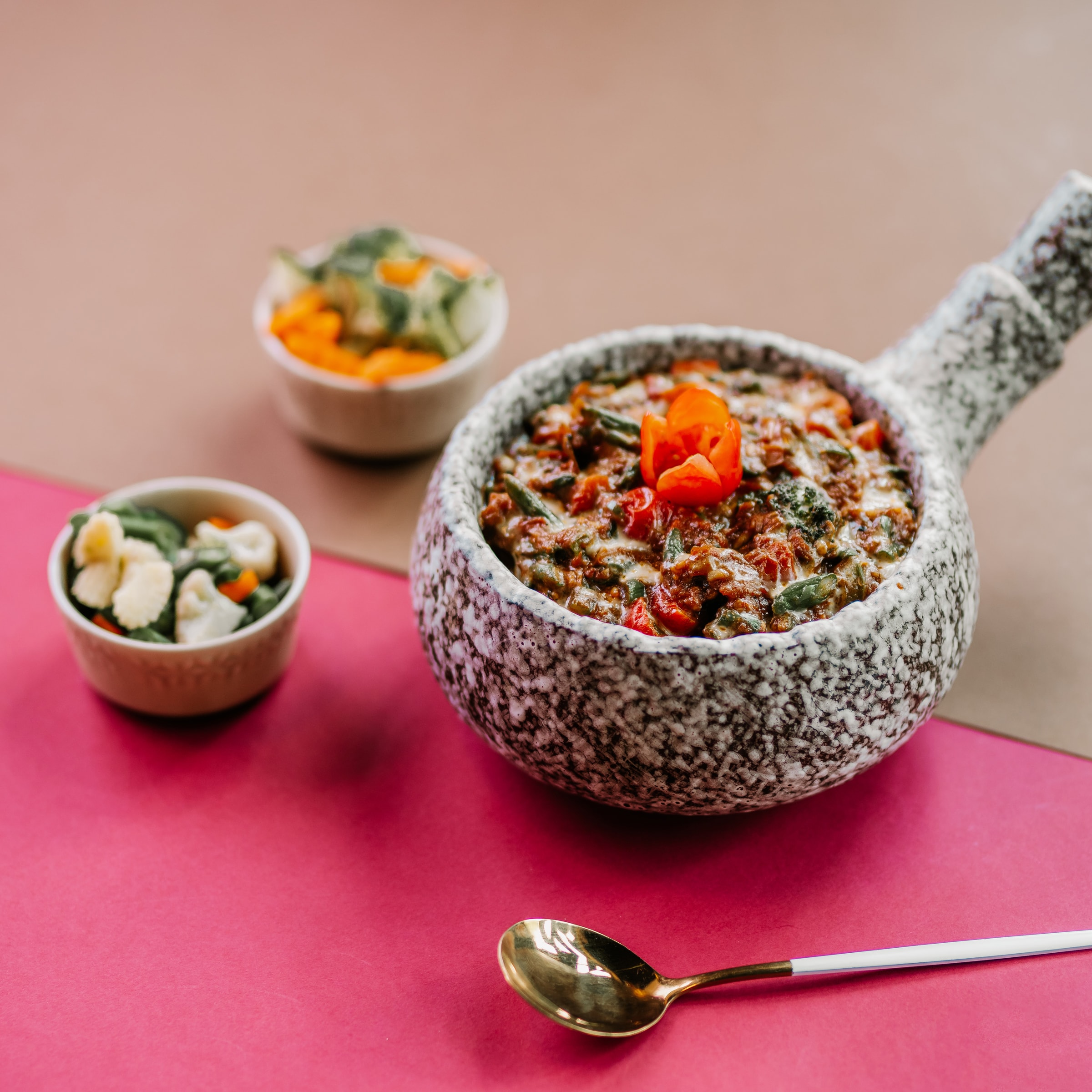 Textured stone pot of curry with small side bowls on pink