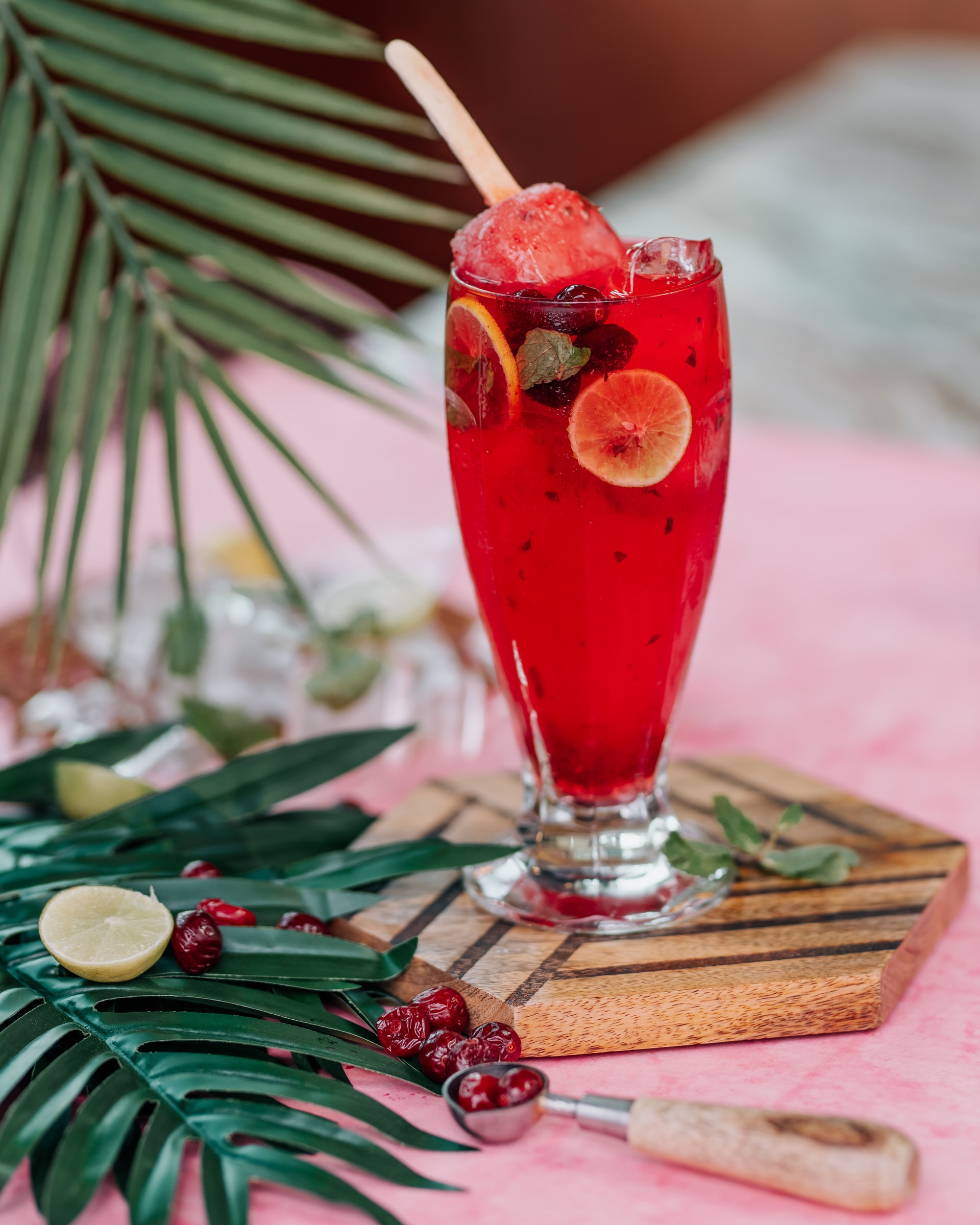 Red iced drink with a popsicle and lime among palm leaves